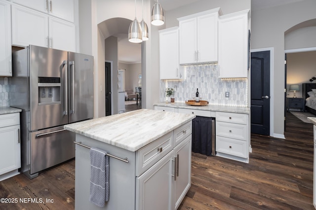 kitchen featuring white cabinets, arched walkways, stainless steel fridge, decorative backsplash, and dark wood-type flooring
