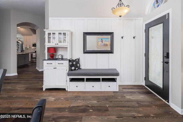mudroom featuring arched walkways, a decorative wall, and dark wood-style flooring