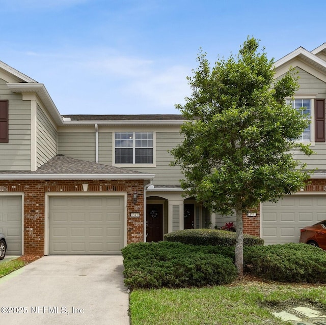 townhome / multi-family property with a shingled roof, driveway, and brick siding