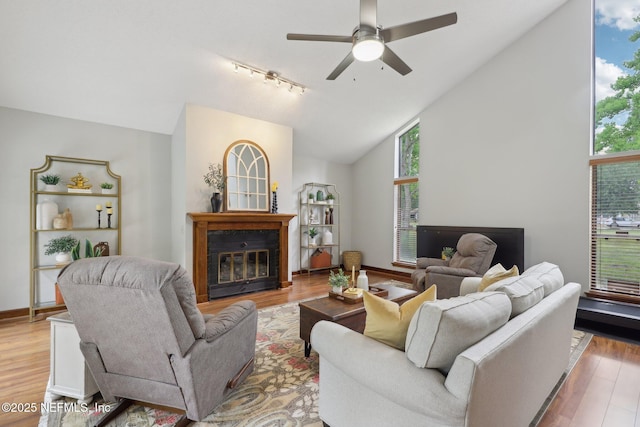 living area featuring rail lighting, a healthy amount of sunlight, light wood-style flooring, and a glass covered fireplace