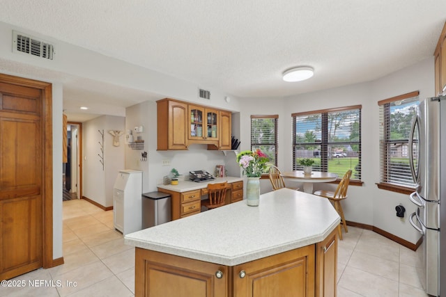 kitchen with freestanding refrigerator, brown cabinets, light countertops, and visible vents
