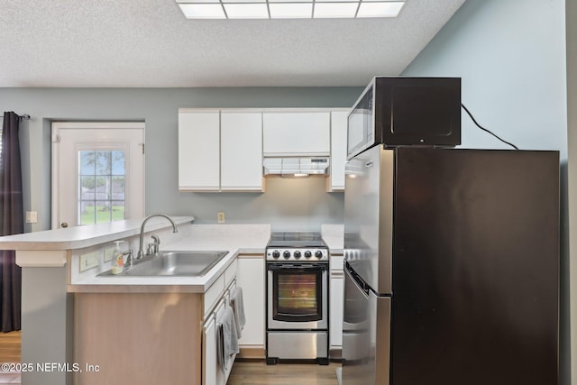 kitchen featuring a sink, a peninsula, under cabinet range hood, light countertops, and appliances with stainless steel finishes
