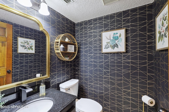 half bath with tile walls, a textured ceiling, toilet, and vanity
