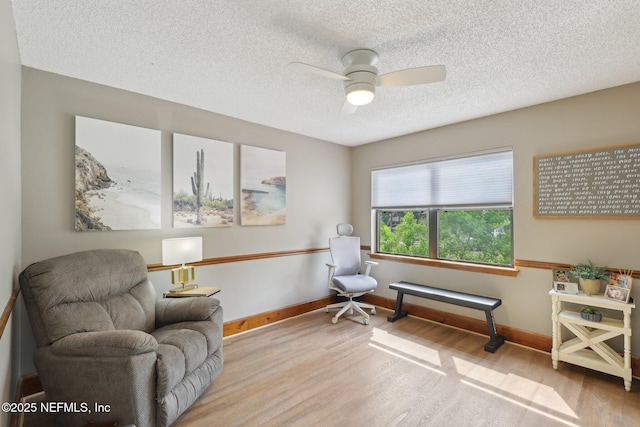 living area with a textured ceiling, baseboards, a ceiling fan, and wood finished floors