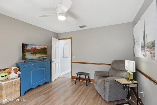 sitting room with light wood-type flooring, visible vents, baseboards, and a ceiling fan