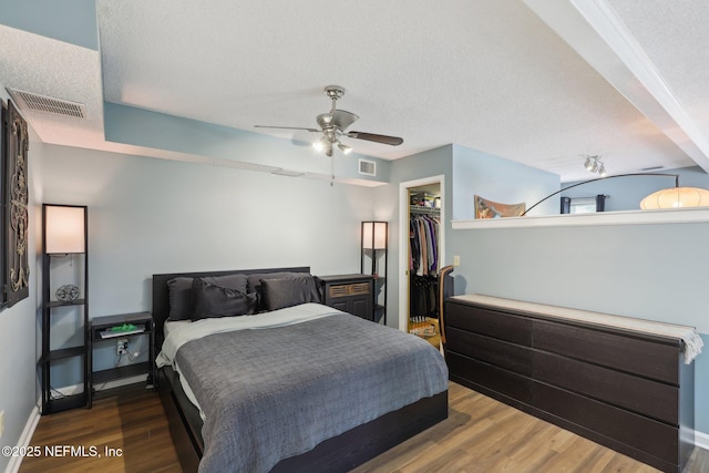 bedroom with a spacious closet, a closet, visible vents, and wood finished floors