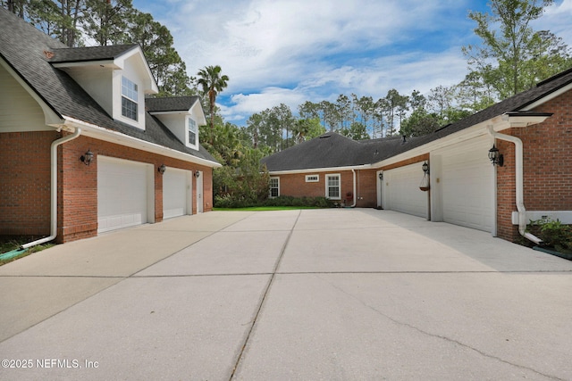 view of side of home featuring concrete driveway, brick siding, a shingled roof, and a garage