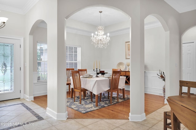 dining area featuring an inviting chandelier, crown molding, baseboards, arched walkways, and light tile patterned floors