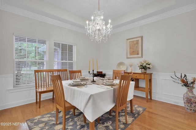 dining room featuring ornamental molding, light wood finished floors, a tray ceiling, and a notable chandelier