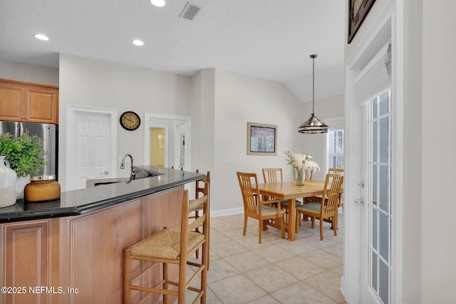 kitchen with dark countertops, a sink, a kitchen breakfast bar, freestanding refrigerator, and visible vents