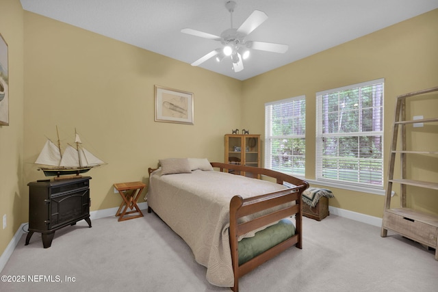 bedroom featuring baseboards, a wood stove, a ceiling fan, and light carpet