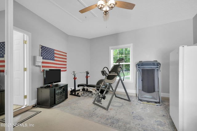 exercise room with baseboards, a ceiling fan, and attic access