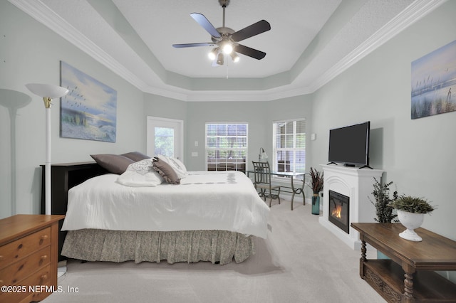 carpeted bedroom with a tray ceiling, a glass covered fireplace, and ceiling fan