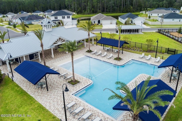 community pool with a yard, a patio area, a forest view, fence, and a residential view