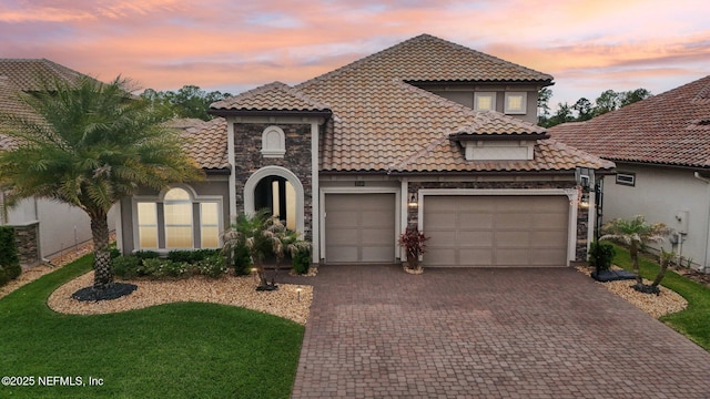 mediterranean / spanish-style house with stone siding, an attached garage, a tiled roof, and decorative driveway