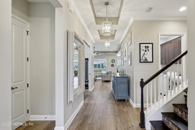 foyer featuring baseboards, visible vents, wood finished floors, stairway, and ornamental molding