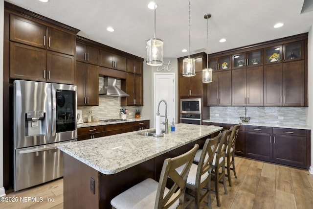 kitchen featuring wall chimney range hood, tasteful backsplash, a sink, dark brown cabinetry, and appliances with stainless steel finishes