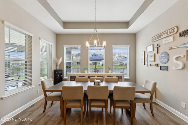 dining area with a tray ceiling, a chandelier, wood finished floors, and baseboards
