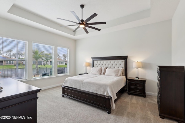 bedroom featuring a raised ceiling, a ceiling fan, baseboards, and light colored carpet
