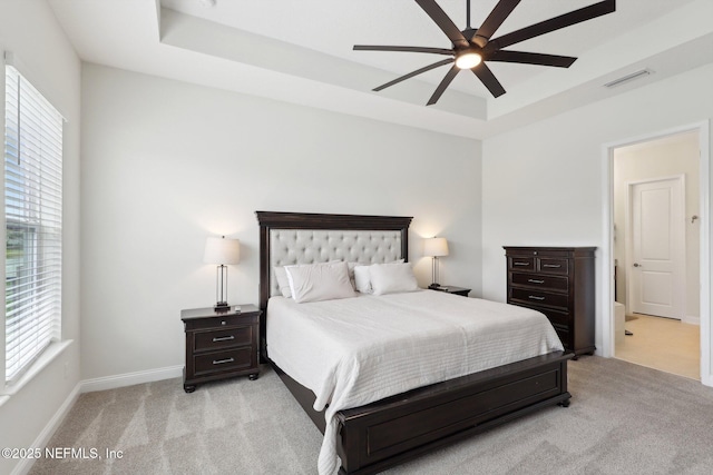 bedroom with a raised ceiling, visible vents, multiple windows, and light carpet