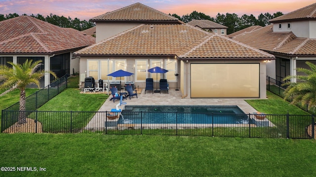 back of house at dusk with a tile roof, a patio area, a lawn, stucco siding, and a fenced backyard
