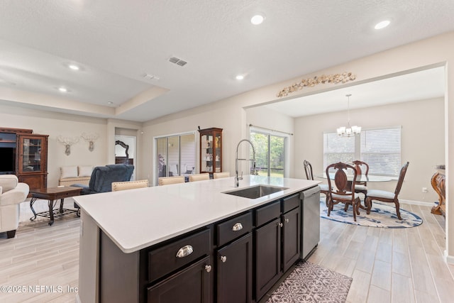 kitchen with a sink, wood tiled floor, open floor plan, light countertops, and visible vents