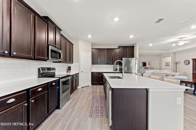 kitchen featuring stainless steel appliances, dark brown cabinets, a sink, light wood-style flooring, and open floor plan