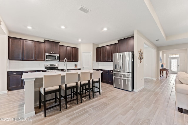 kitchen with dark brown cabinets, decorative backsplash, a breakfast bar, light countertops, and appliances with stainless steel finishes