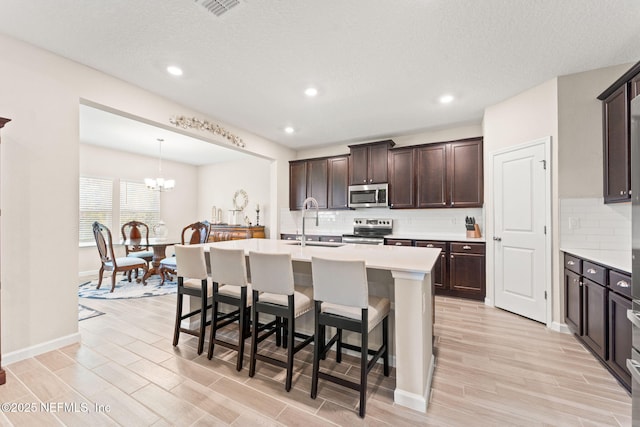 kitchen with backsplash, appliances with stainless steel finishes, a sink, and light wood-style floors