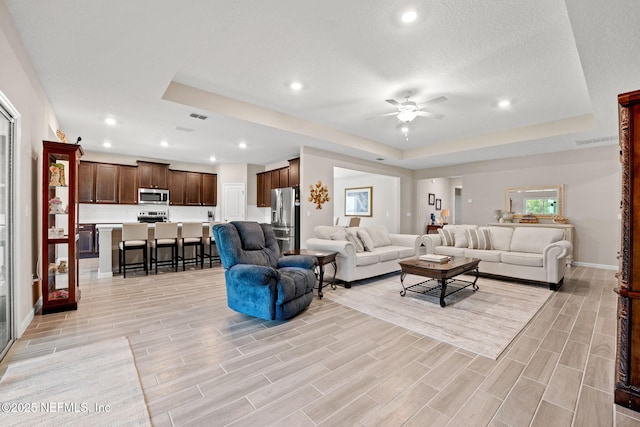 living room with ceiling fan, recessed lighting, light wood-style floors, and a raised ceiling