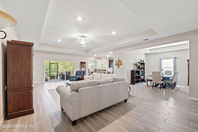 living room with baseboards, a ceiling fan, a textured ceiling, and a raised ceiling