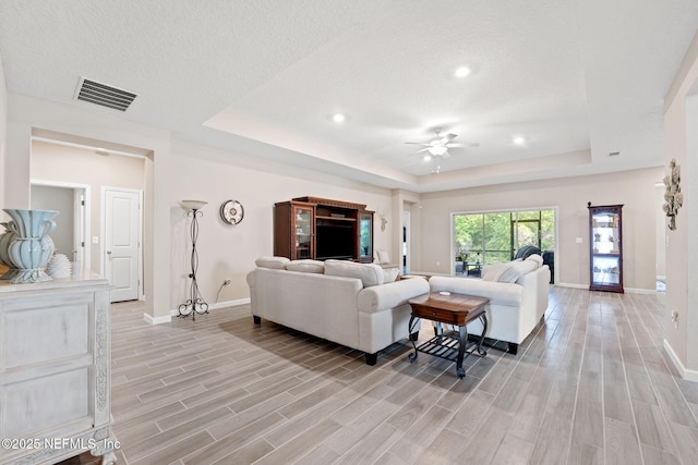 living room with baseboards, a ceiling fan, visible vents, and a raised ceiling