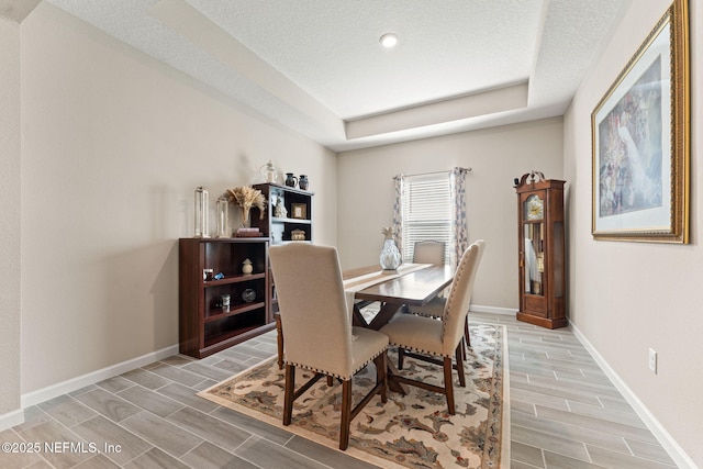 dining space with a textured ceiling, a raised ceiling, wood finish floors, and baseboards