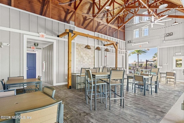 dining area with wood finished floors, a decorative wall, high vaulted ceiling, and ceiling fan