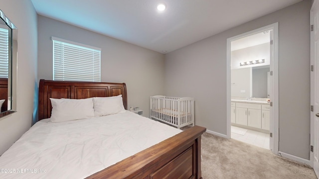 bedroom with light carpet, ensuite bath, and baseboards