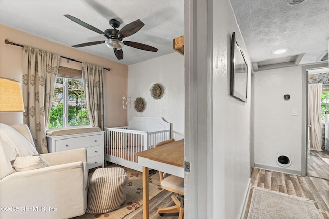 bedroom featuring a textured ceiling, wood finished floors, a nursery area, and multiple windows