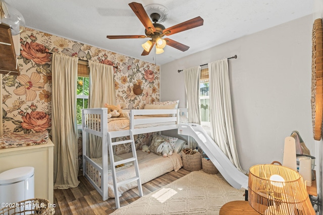 bedroom featuring ceiling fan, multiple windows, wallpapered walls, and wood finished floors