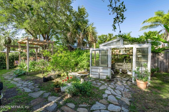 view of yard featuring an outdoor structure, a pergola, fence, an exterior structure, and a vegetable garden