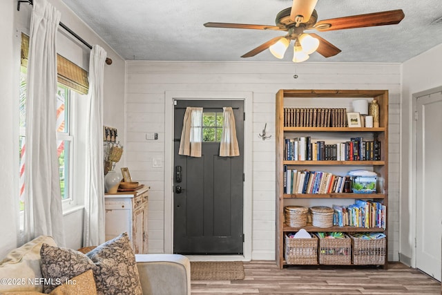 entryway featuring wooden walls, a textured ceiling, a ceiling fan, and wood finished floors