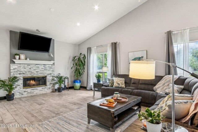 living area featuring baseboards, recessed lighting, a fireplace, wood finished floors, and high vaulted ceiling