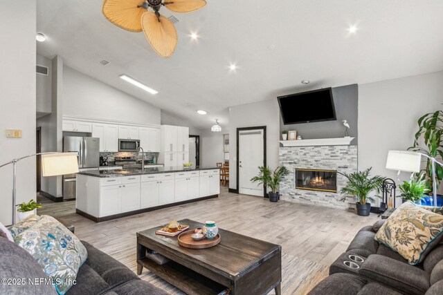 living room featuring a tile fireplace, light wood-type flooring, visible vents, a ceiling fan, and lofted ceiling
