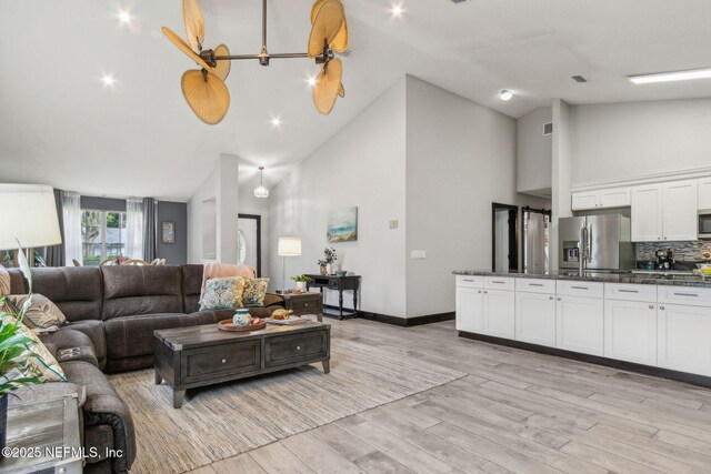 living area featuring light wood finished floors, visible vents, high vaulted ceiling, and baseboards
