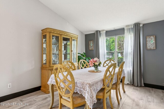 dining space with baseboards, light wood-style floors, and lofted ceiling