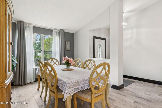 dining area with baseboards, vaulted ceiling, and light wood-style floors