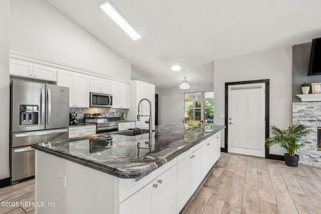 kitchen featuring a sink, backsplash, white cabinets, appliances with stainless steel finishes, and an island with sink
