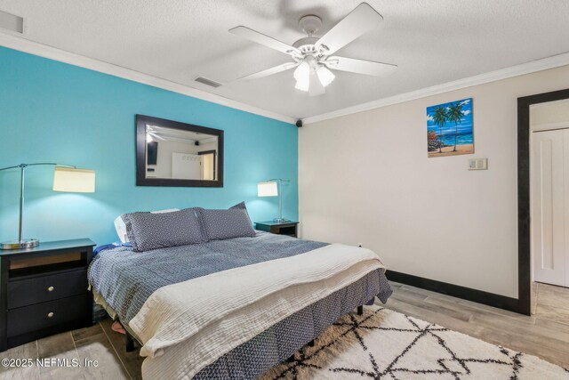 bedroom featuring ceiling fan, visible vents, baseboards, ornamental molding, and wood finished floors