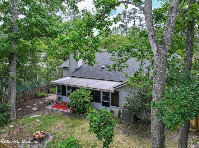 back of property with a chimney, a fenced backyard, a shingled roof, a sunroom, and cooling unit