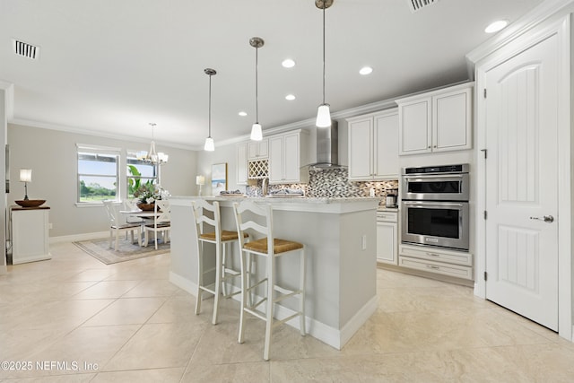 kitchen featuring wall chimney range hood, stainless steel double oven, visible vents, tasteful backsplash, and ornamental molding
