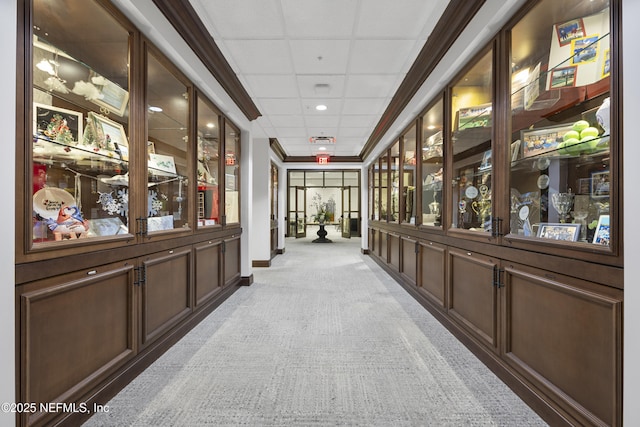 hall featuring baseboards, a drop ceiling, and light carpet