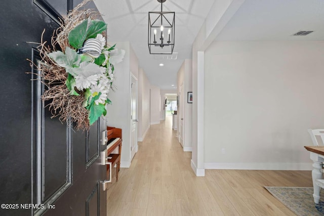 corridor featuring baseboards, visible vents, light wood-style floors, and a notable chandelier